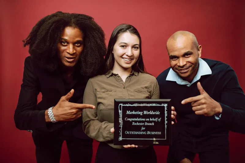 Three diverse professionals proudly pose with an award for outstanding business achievement.