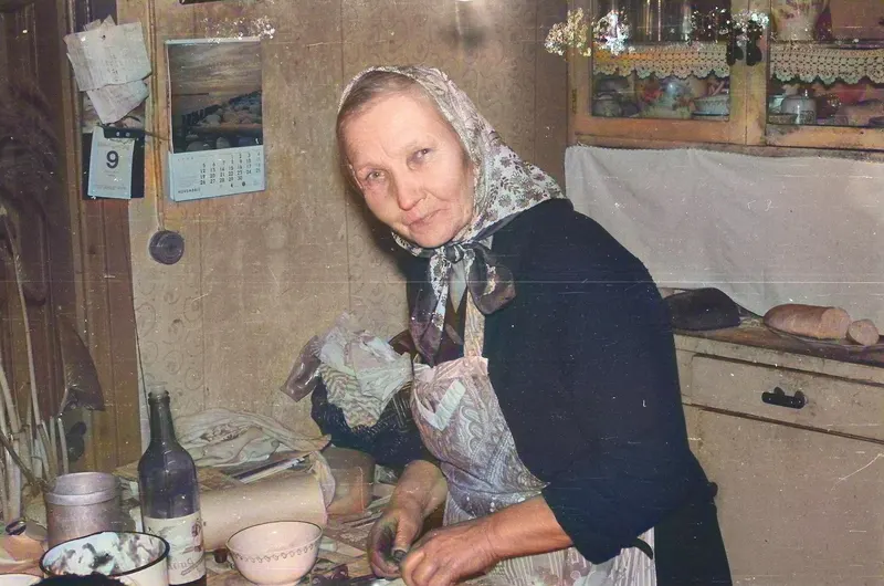 Senior woman in traditional attire cooking in a cozy kitchen in Latvia.