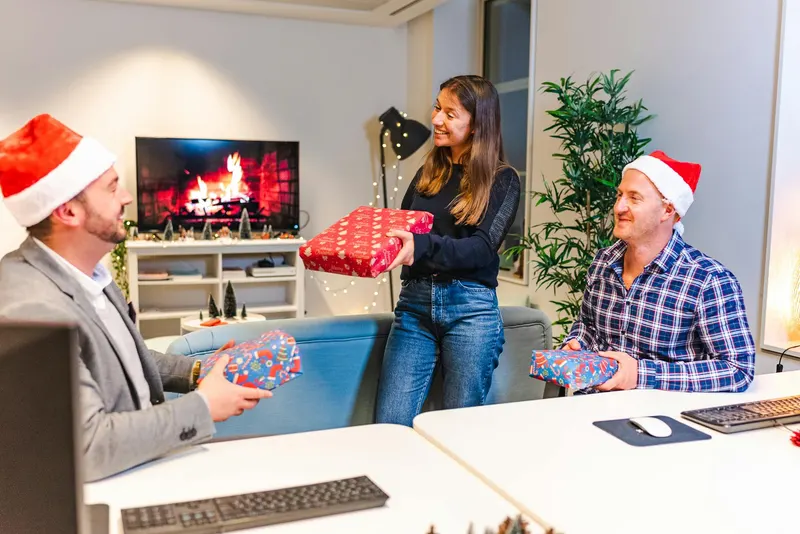 Colleagues exchanging gifts in an office with Christmas decorations.