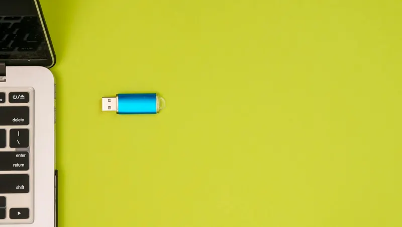 A blue USB drive next to a laptop on a vibrant yellow background showcasing portable technology.