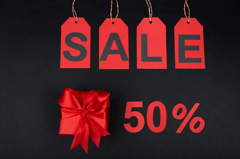 Red gift box next to sale tags and 50% sign on black background, ideal for promotions.
